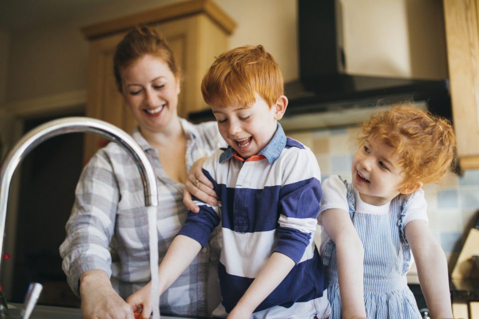 Two children and their Mother washing the dishes in the kitchen sink.