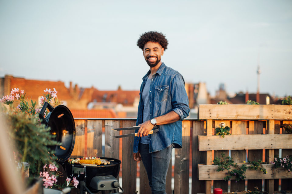 Male cooking on barbecue grill by railing on rooftop.