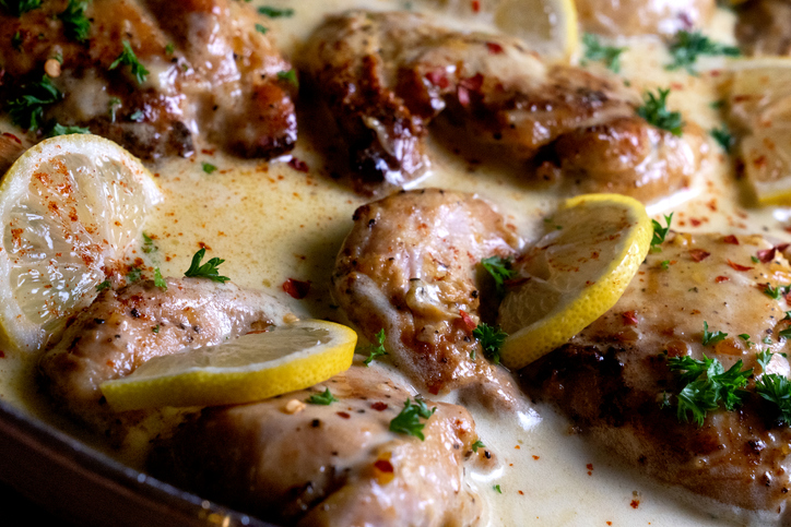 lemon cream chicken seared in a pan with lemon slices and a creamy garlic sauce