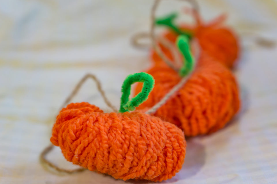 craft pumpkins made of orange yarn and green pipe cleaner