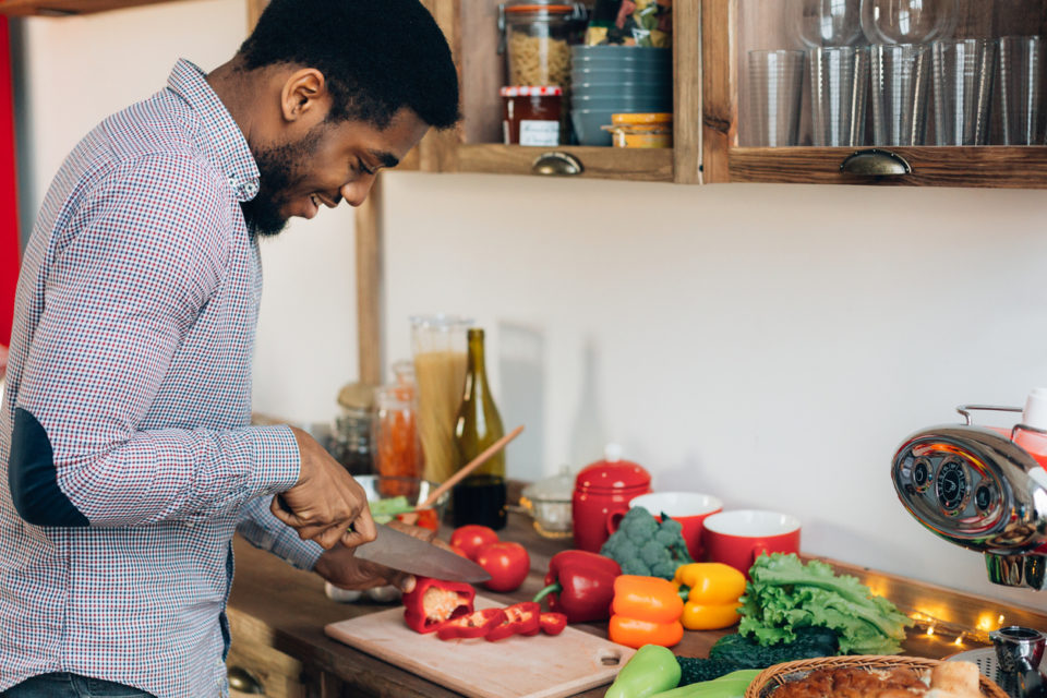 Man preparing delicious food in kitchen, cutting fresh vegetables