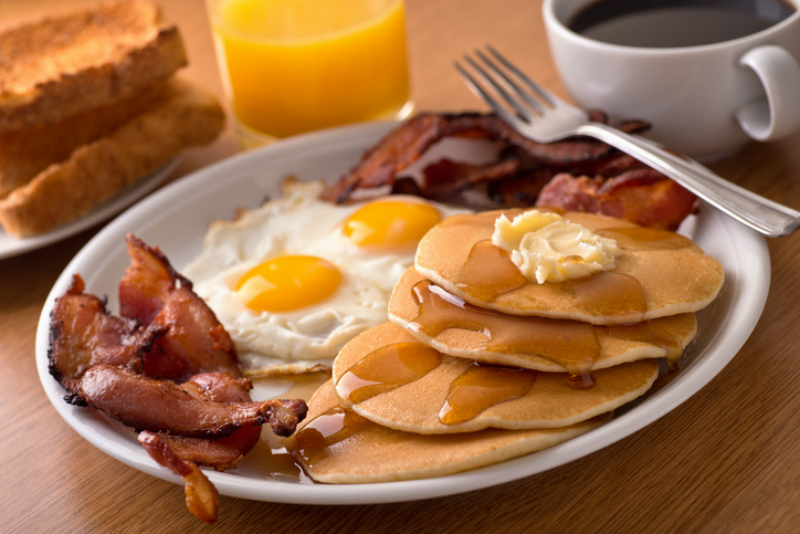 A delicious home style breakfast with crispy bacon, eggs, pancakes, toast, coffee, and orange juice.