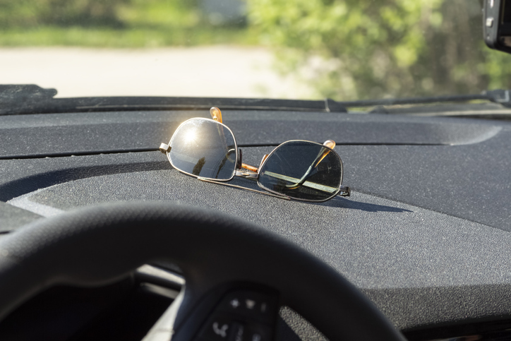Sunglasses lie on the dashboard of a car while waiting for a ride.